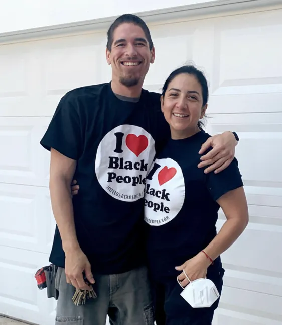 Smiling man and woman standing close together, both wearing black T-shirts with 'I love Black People' printed on the front.
