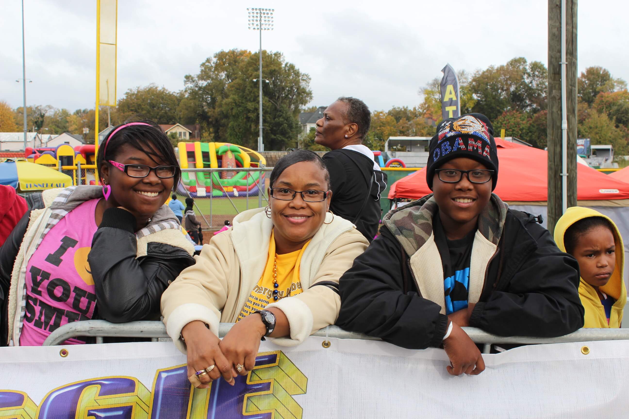 Smiling group of four people standing behind a fence at an outdoor event with colorful inflatables in the background.