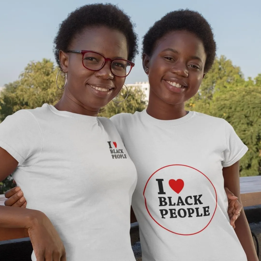 Two smiling Black women standing close together outdoors, wearing white shirts that say 'I ♥ BLACK PEOPLE'.