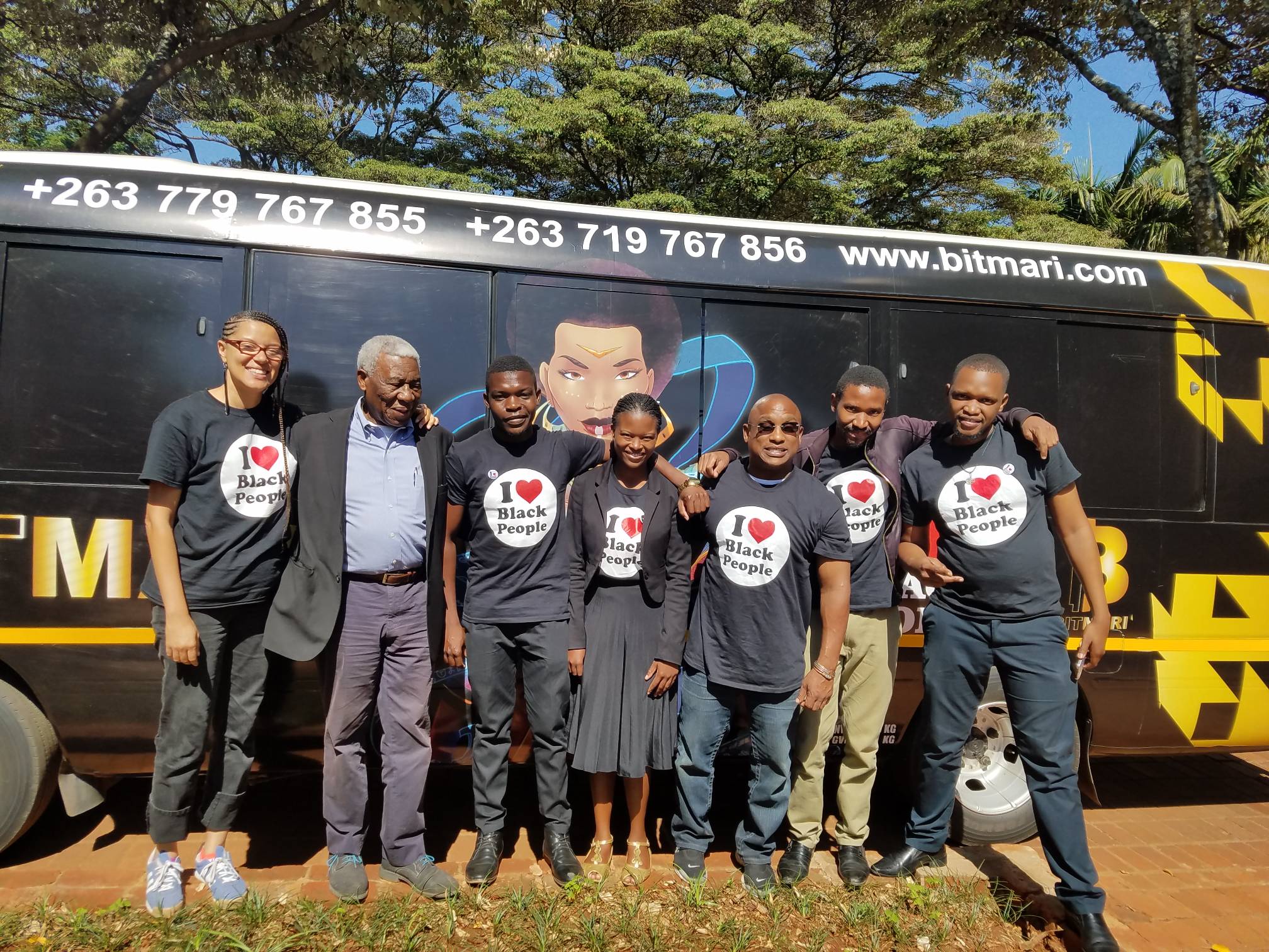 Group of seven people standing in front of a black vehicle with contact numbers and website, five wearing black t-shirts that say 'I love Black People.'