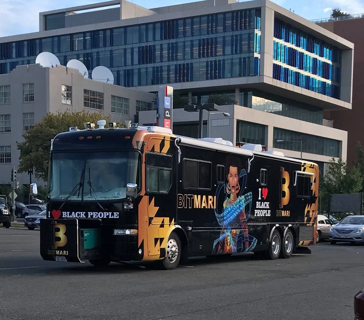 Black bus with orange geometric design and an illustration of a woman, displaying the text 'I ♥ BLACK PEOPLE' and 'BITMARI' on the side.