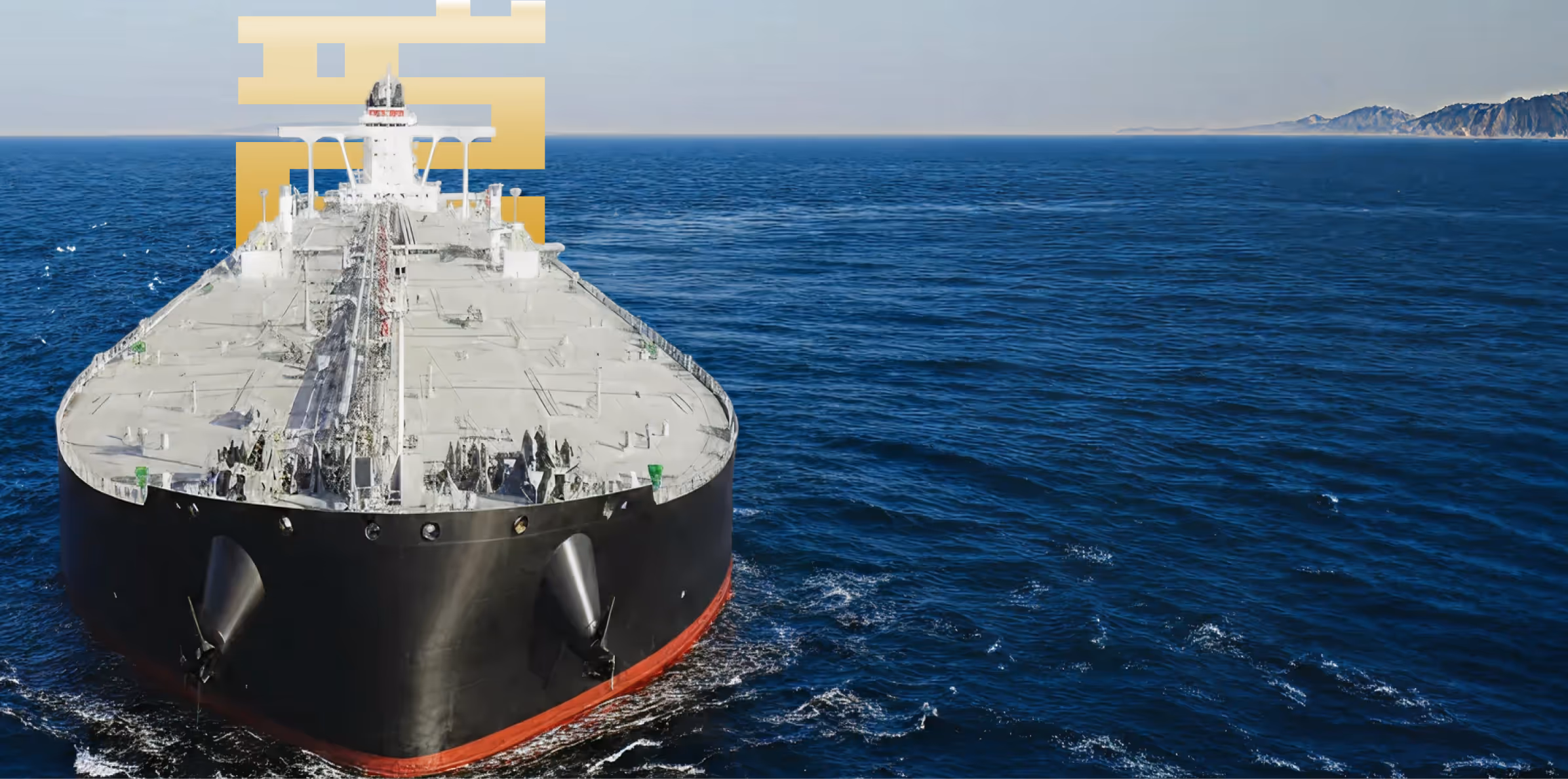 Large black and red oil tanker ship sailing on a calm blue sea with a distant coastline on the right.