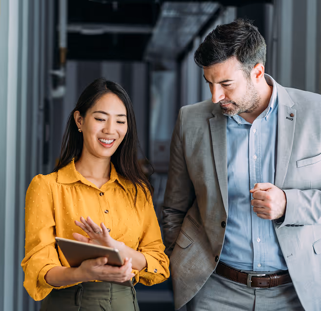 Smiling woman in yellow blouse showing a tablet to a man in a grey suit indoors.