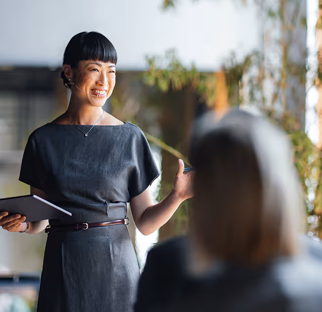 Smiling woman with headset microphone holding a tablet and speaking to an audience.