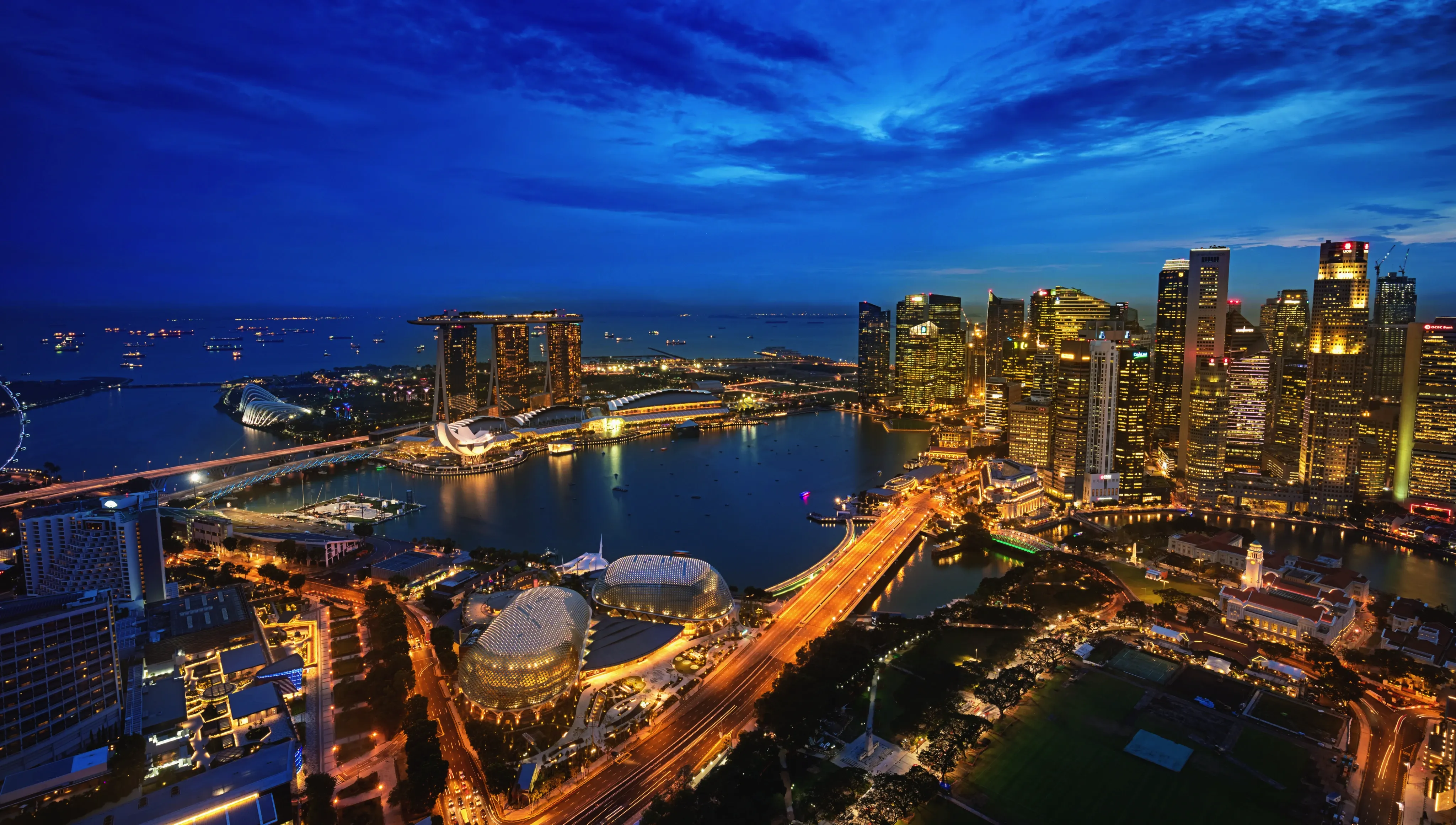 Night aerial view of Singapore skyline with Marina Bay Sands, waterfront, and illuminated city buildings.