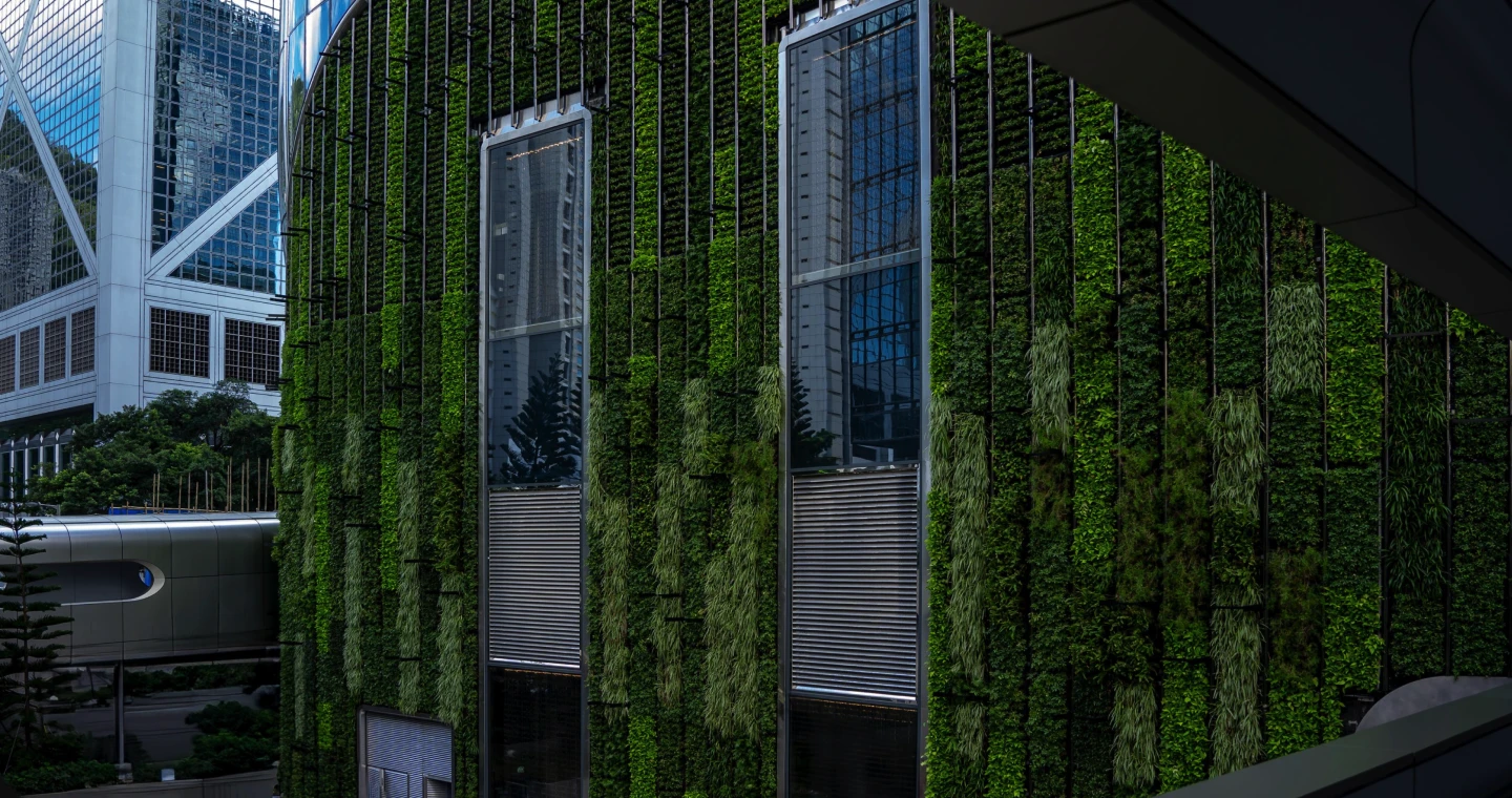 Building facade covered in vertical green plants with windows reflecting nearby skyscrapers.