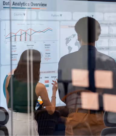 Two professionals analyzing a digital data analytics dashboard projected on a screen with charts and metrics.