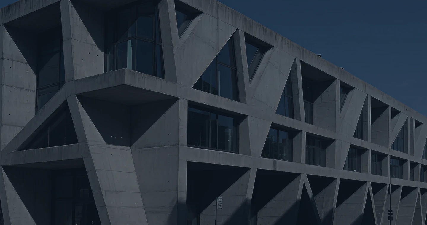 Modern concrete building with geometric triangular window frames under a clear blue sky.