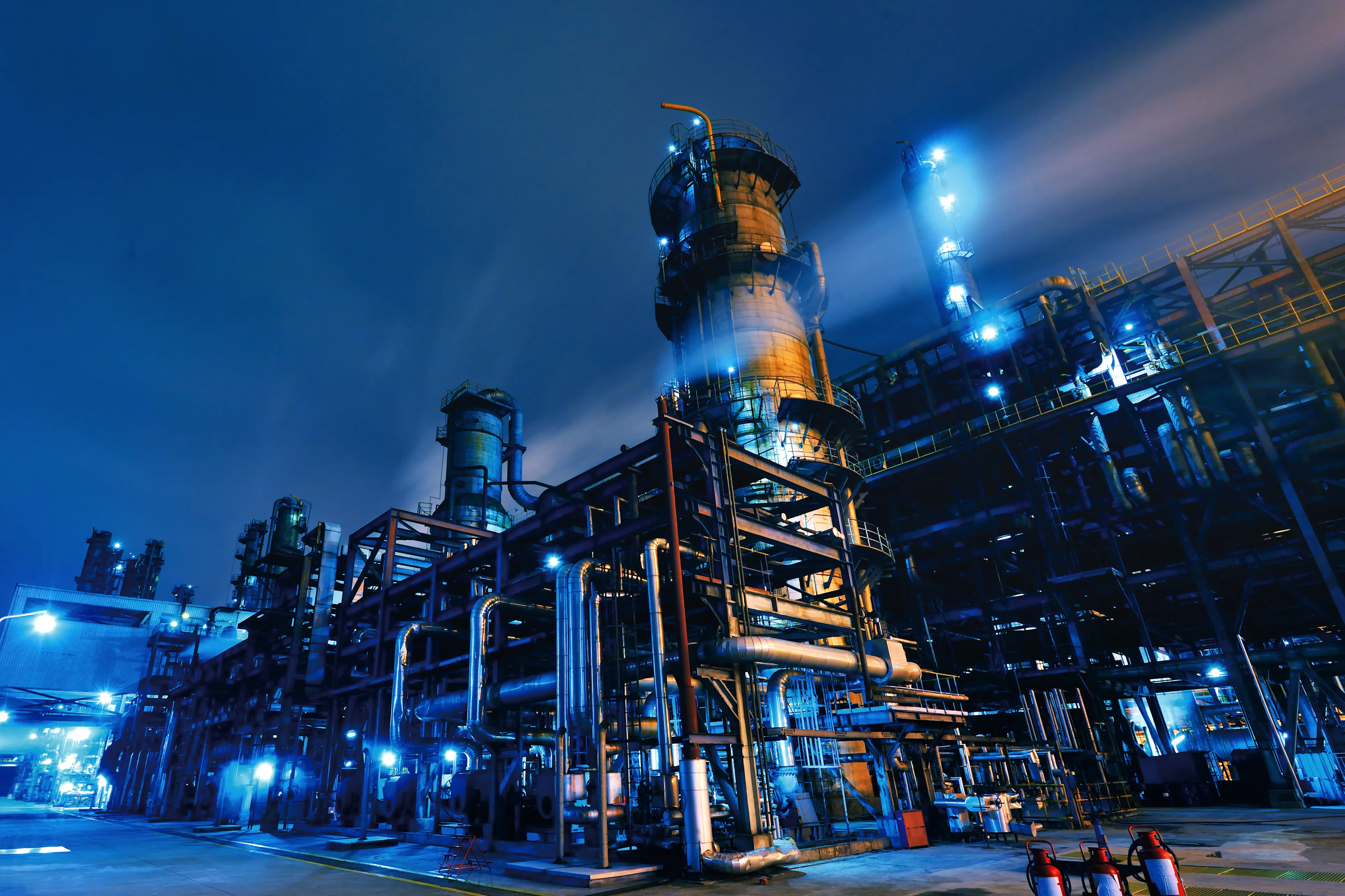 Industrial refinery plant illuminated with blue lights at night under a dark sky.