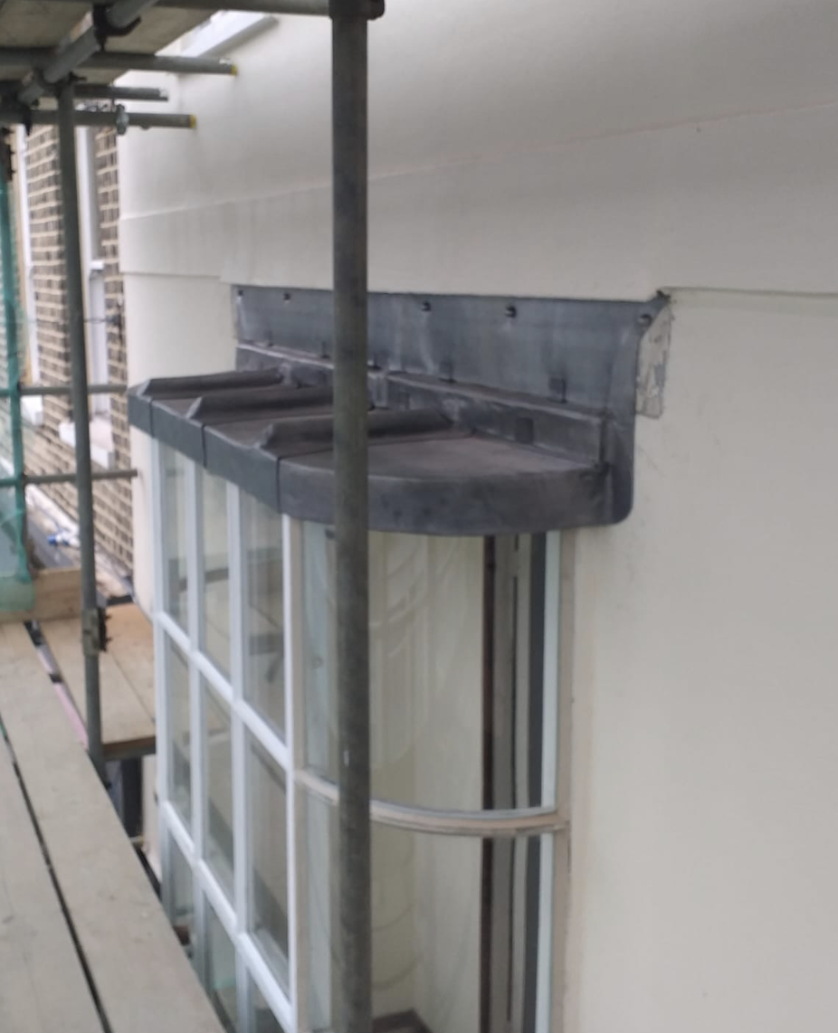 Curved glass window with a metal canopy above, viewed from scaffolding.