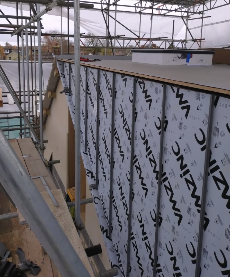 Construction site view of a building facade being insulated with WIZINC panels, surrounded by scaffolding.