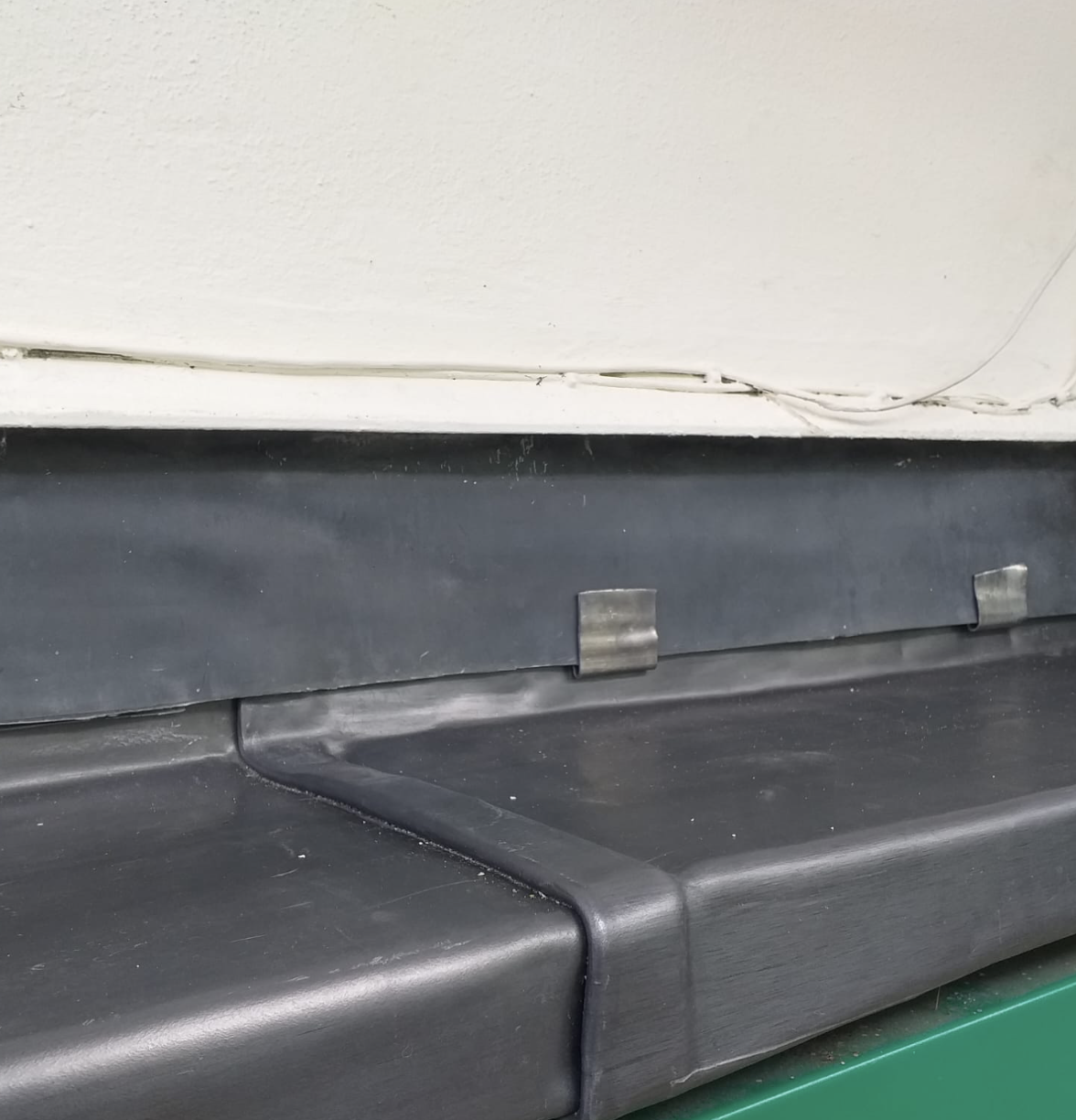 Close-up of a black rubber baseboard with two metal clips mounted on a white wall above a green surface.