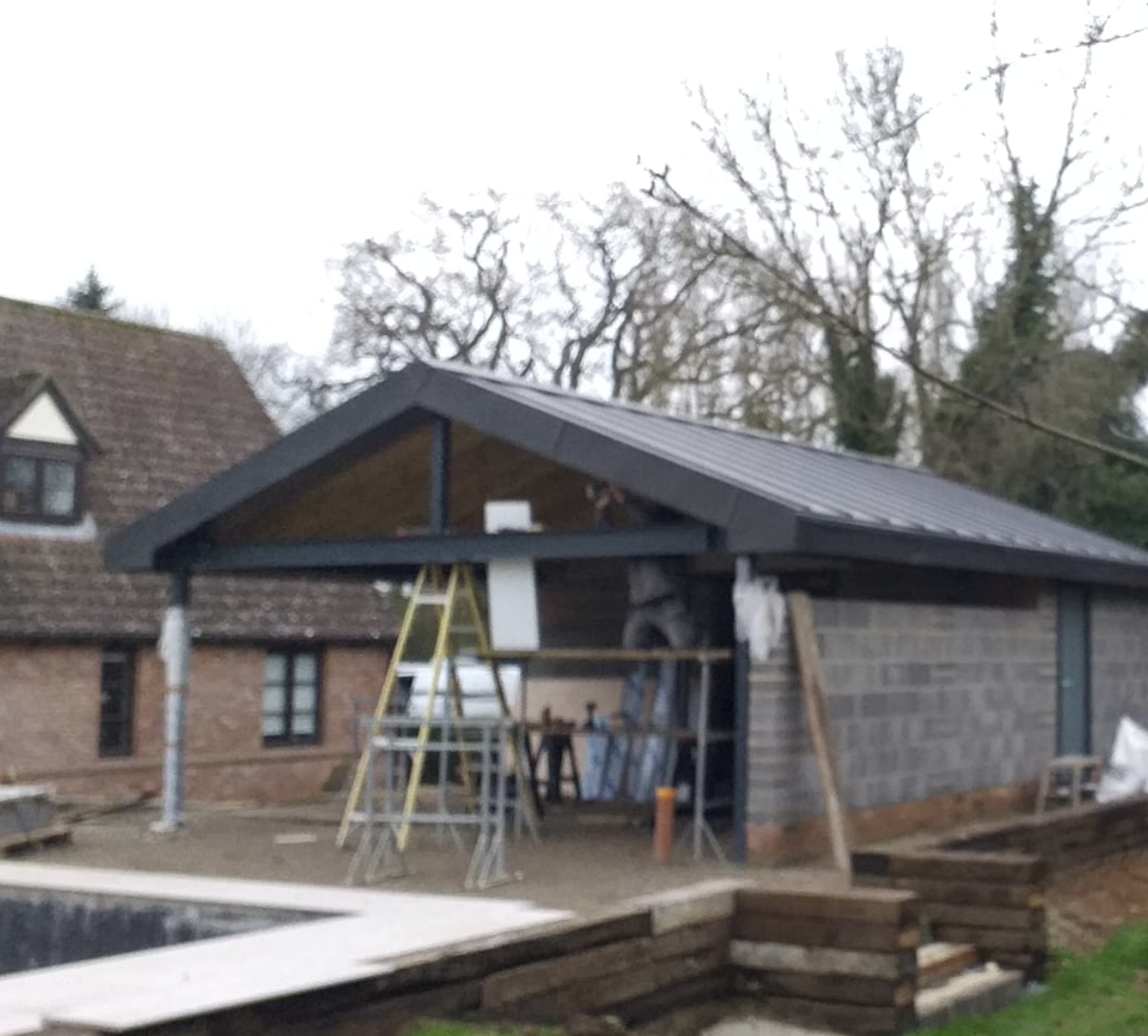 Outdoor construction site with a partially built shelter featuring a metal roof and scaffolding.