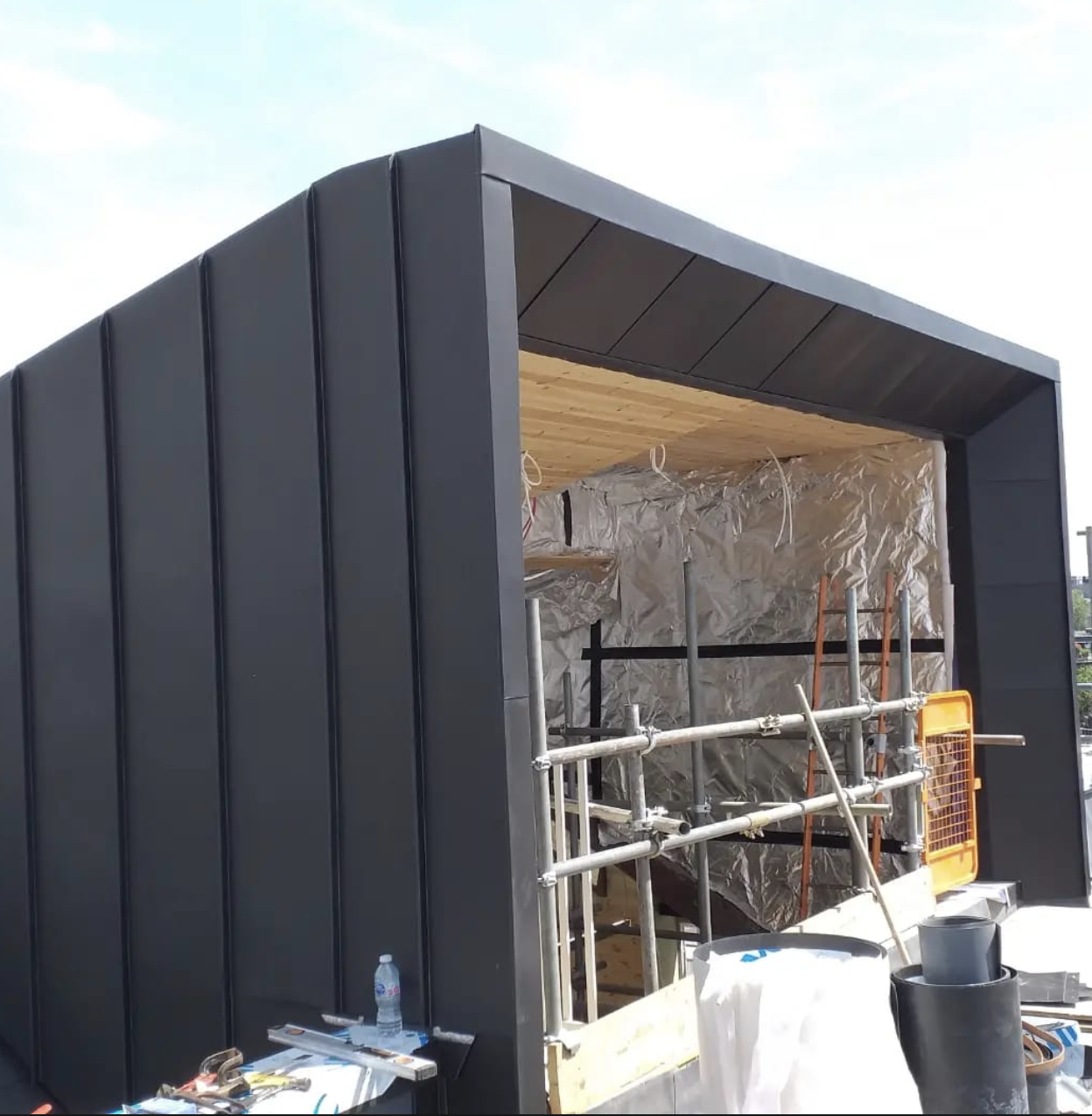 Under-construction modern black modular building with scaffolding and construction materials inside.