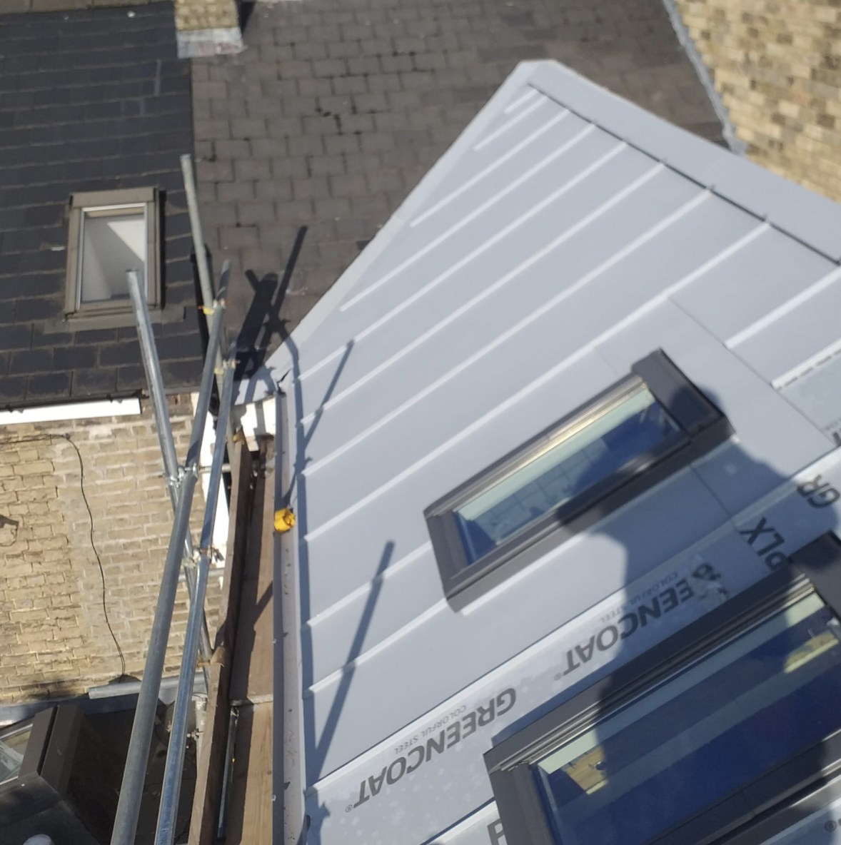 Roof under construction with metal panels and two skylight windows, scaffolding on the side.