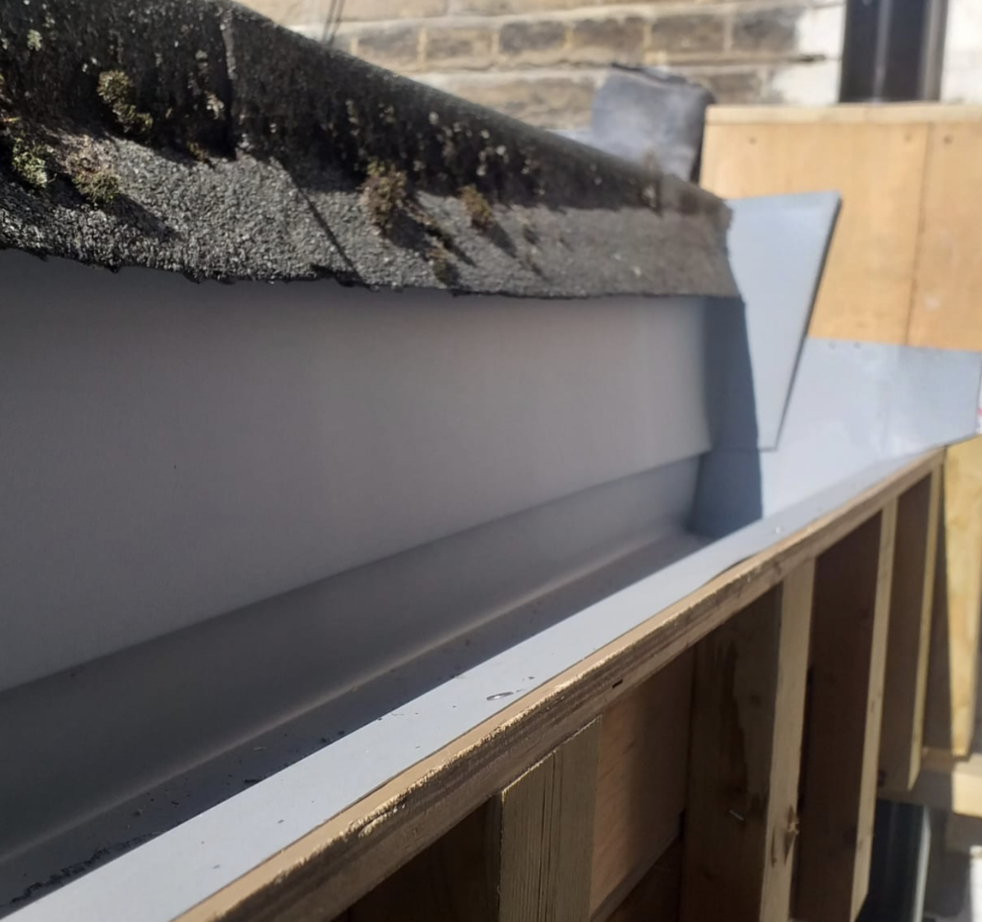 Close-up of a clean white rain gutter installed on a roof edge with wooden framing below.