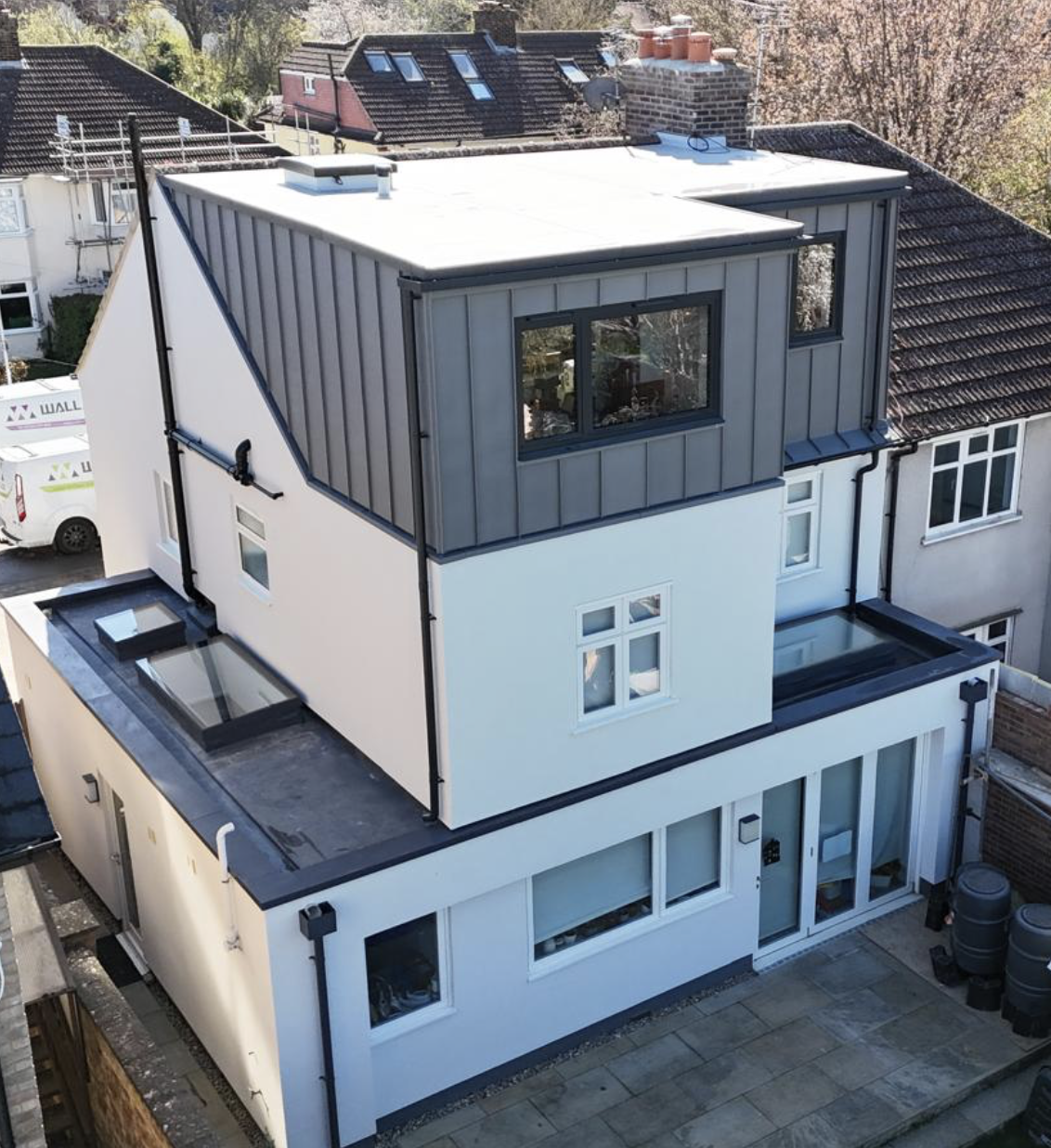 Modern two-story house with white walls and gray vertical cladding on the upper floor, featuring multiple windows and a flat roof.