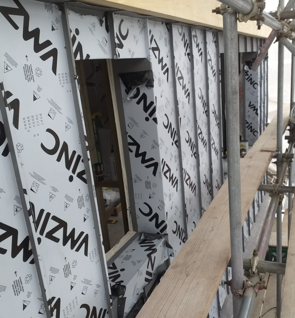 Construction site scaffolding next to a building wall covered with VIZWA insulation panels, with window frames partially installed.