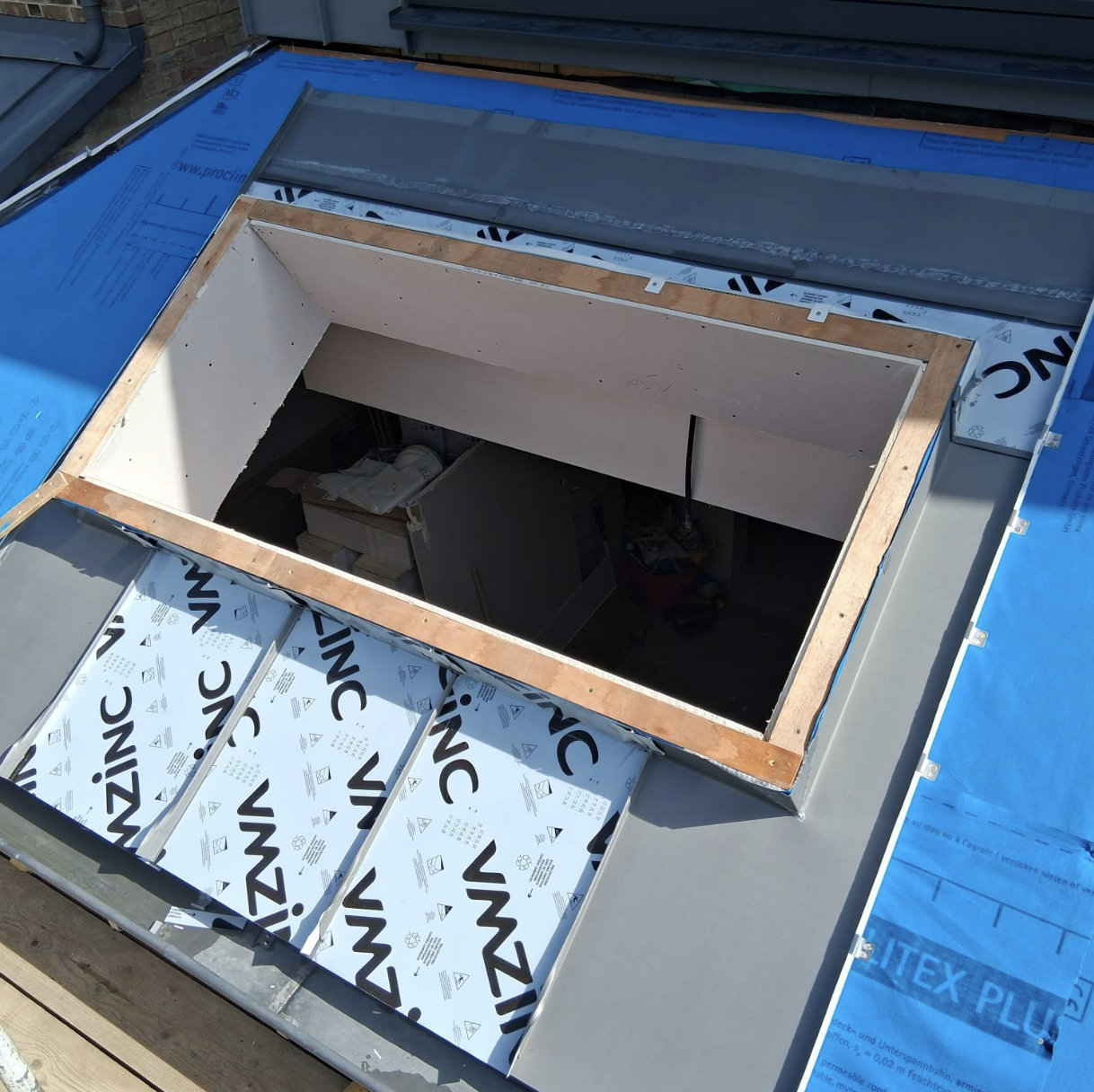Roof under construction with a rectangular skylight frame and VMZINC metal panels partially installed around it.