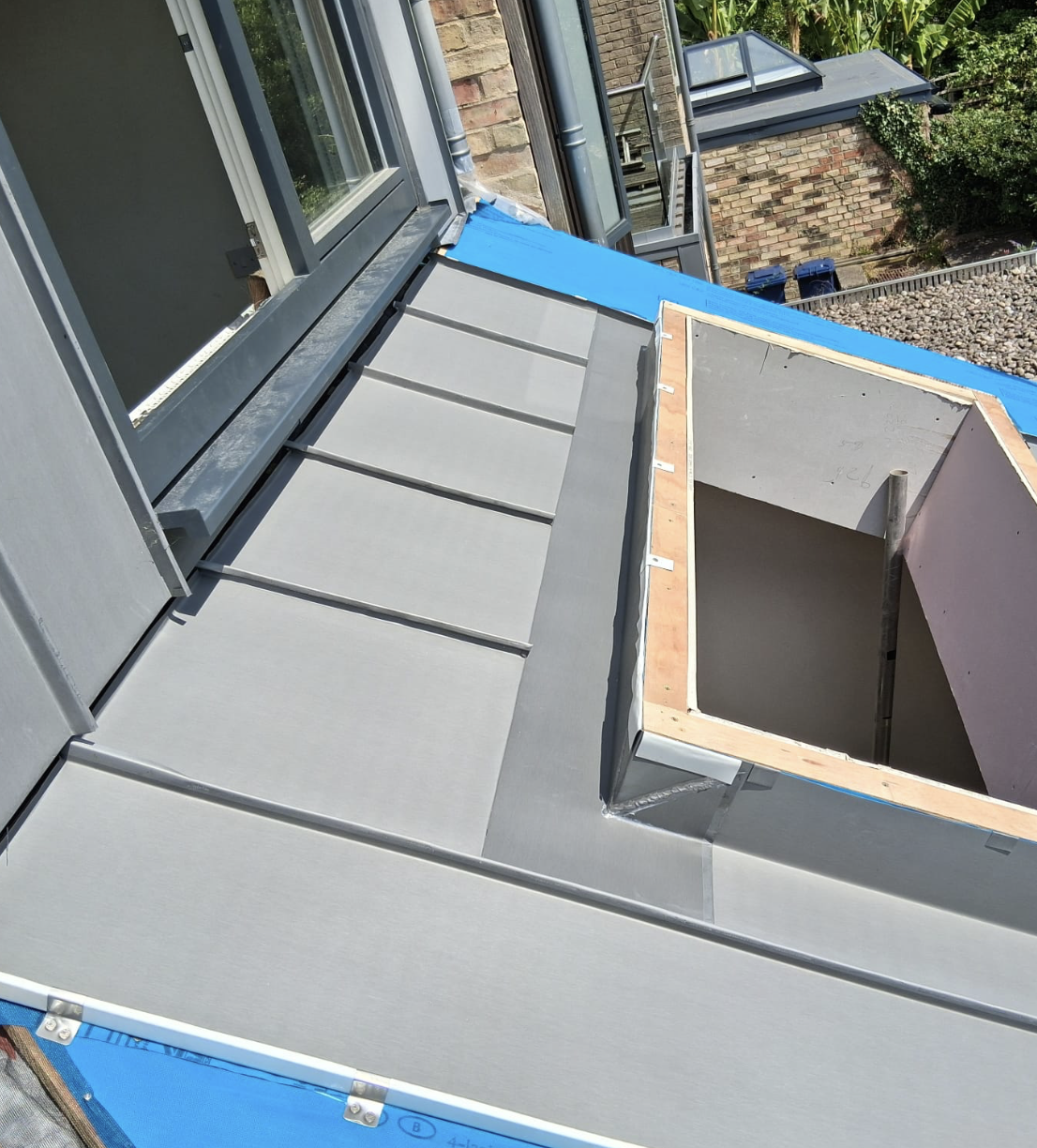 Close-up of a newly installed flat metal roof section with a framed skylight opening next to an open window.