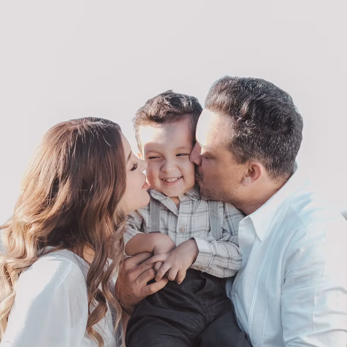 Mother and father kissing their smiling young son on the cheeks in a close family portrait.