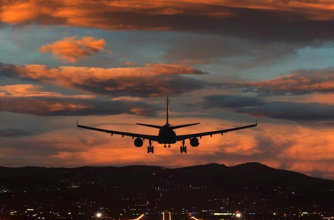 Airplane landing at sunset with illuminated runway and mountains in the background.