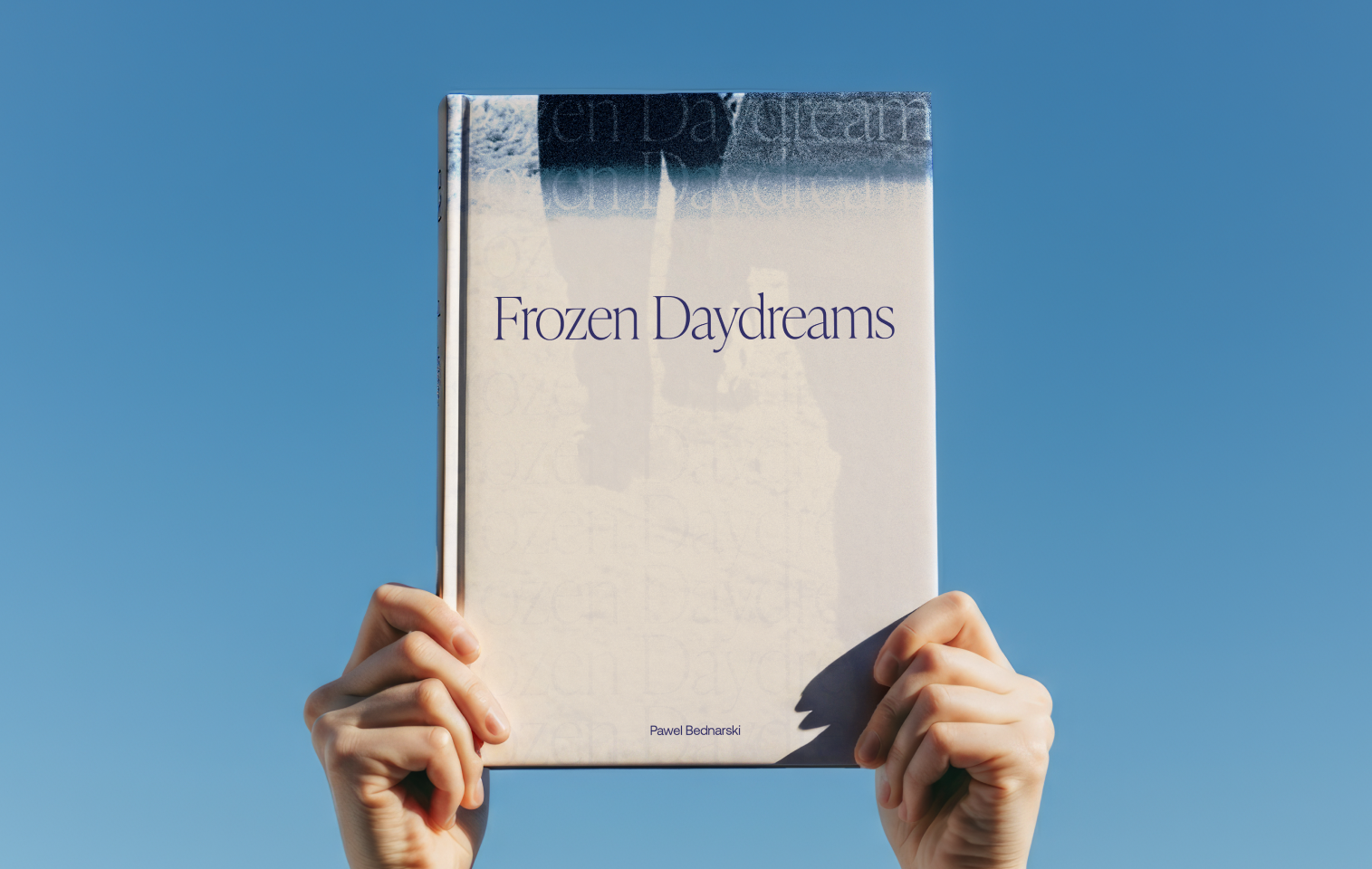 Frozen Daydreams photobook held up in the sky.