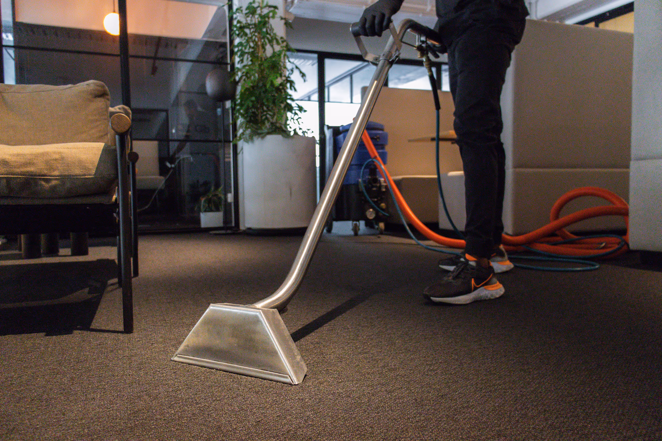 Person using a professional carpet cleaning machine with hoses in an office setting.