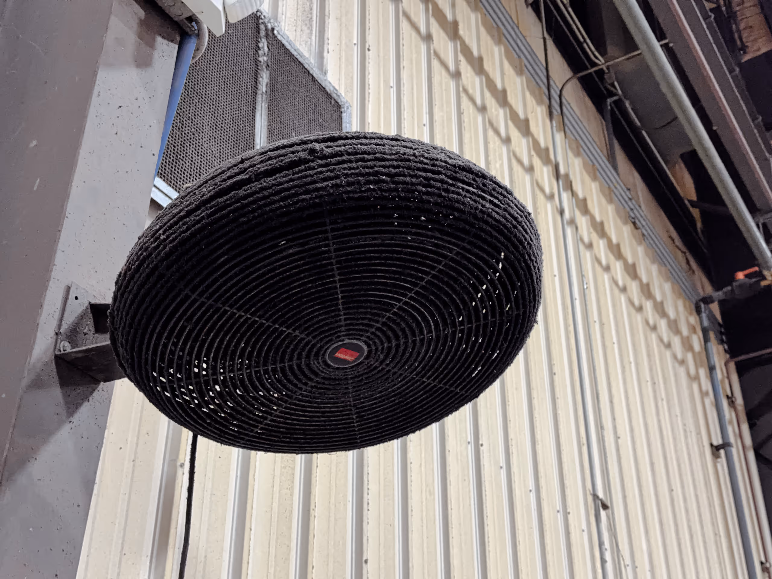 Large industrial black circular ventilation fan mounted on a metal wall inside a warehouse.