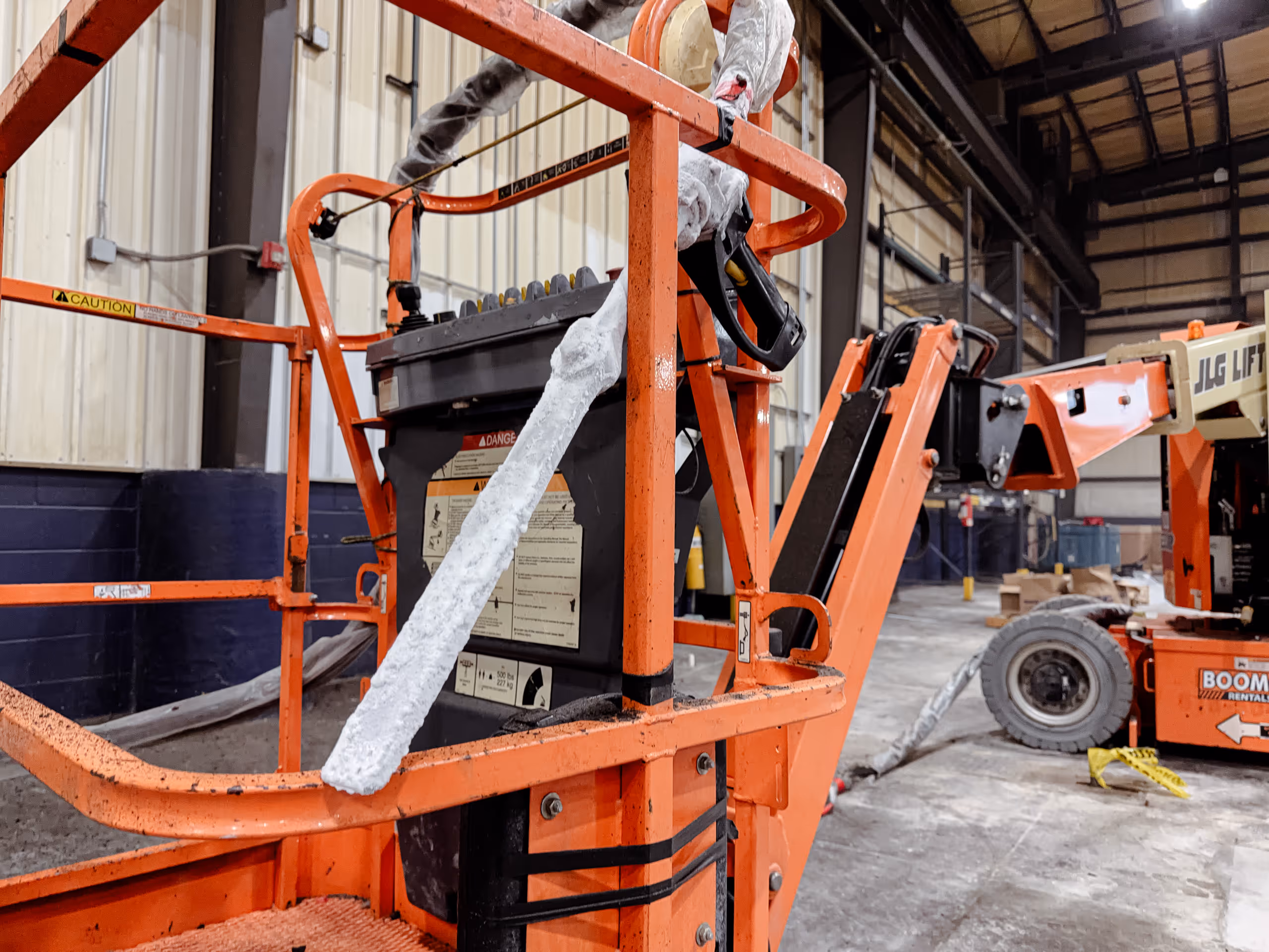Close-up of an orange boom lift in an industrial warehouse with foam insulation wrapped on parts of the lift.