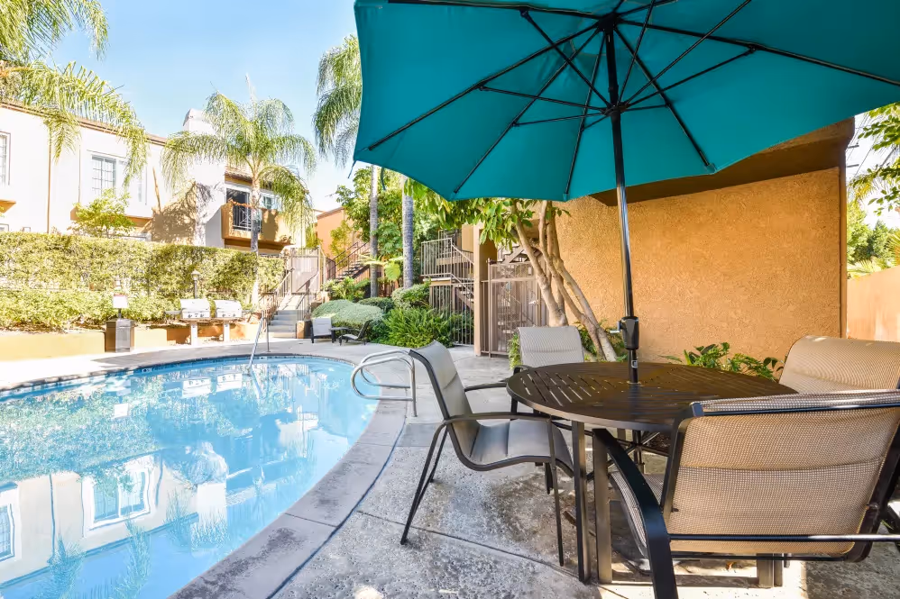picnic table with umbrella in front of swimming pool