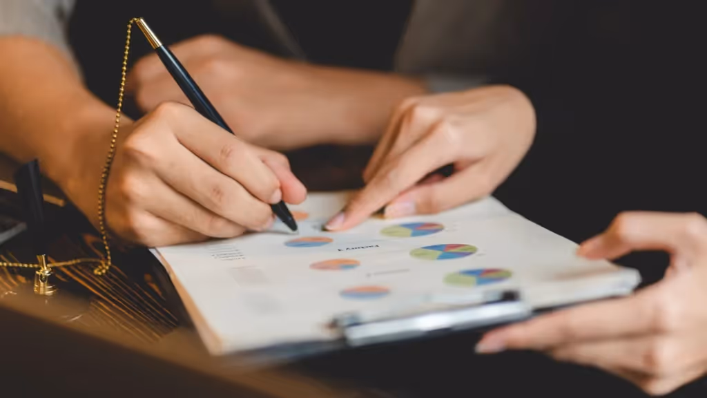 Two people are discussing some charts on a clipboard. One of them is holding a pen.