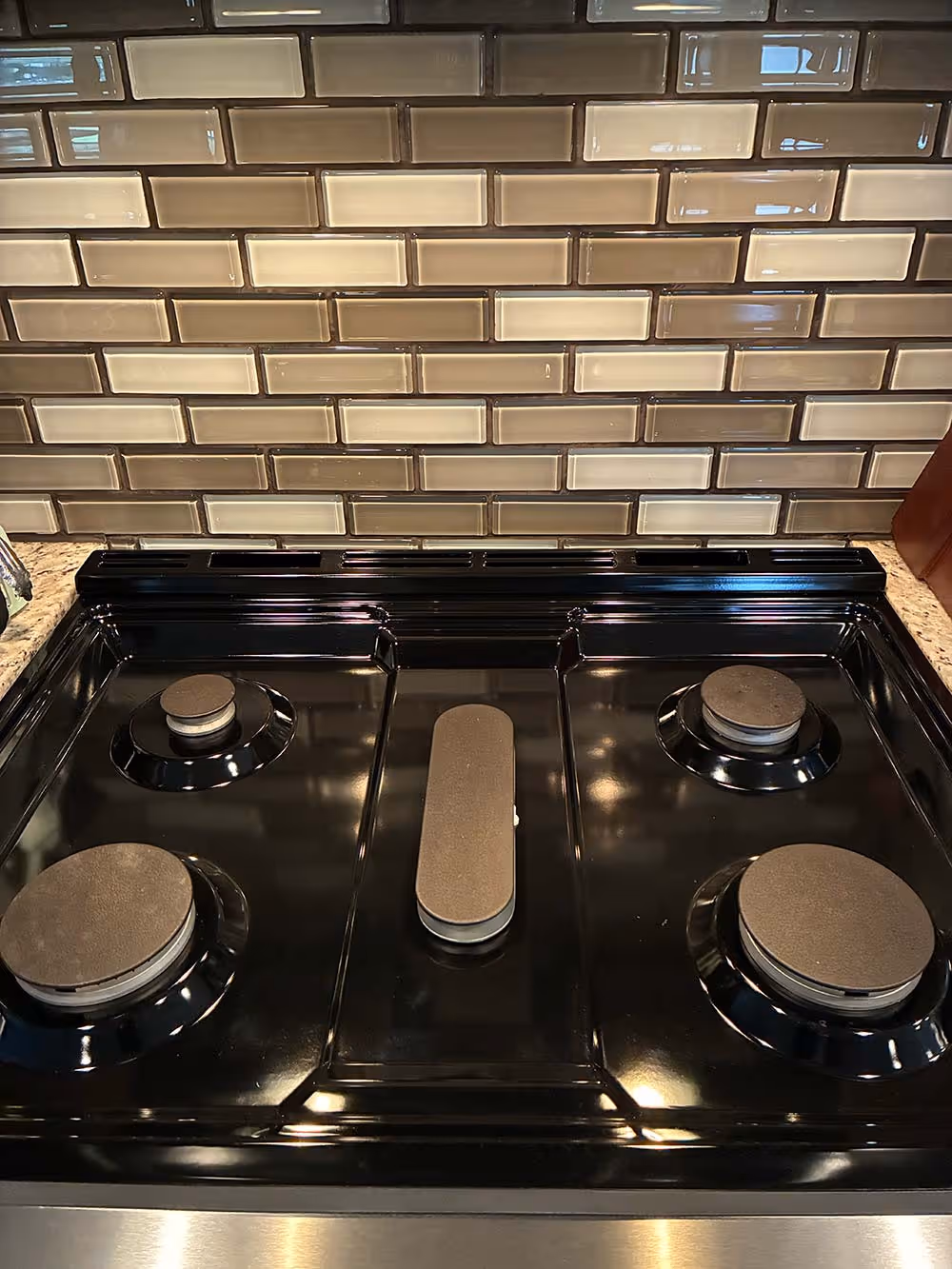 Clean black gas stove with four burners against a beige and brown subway tile backsplash.