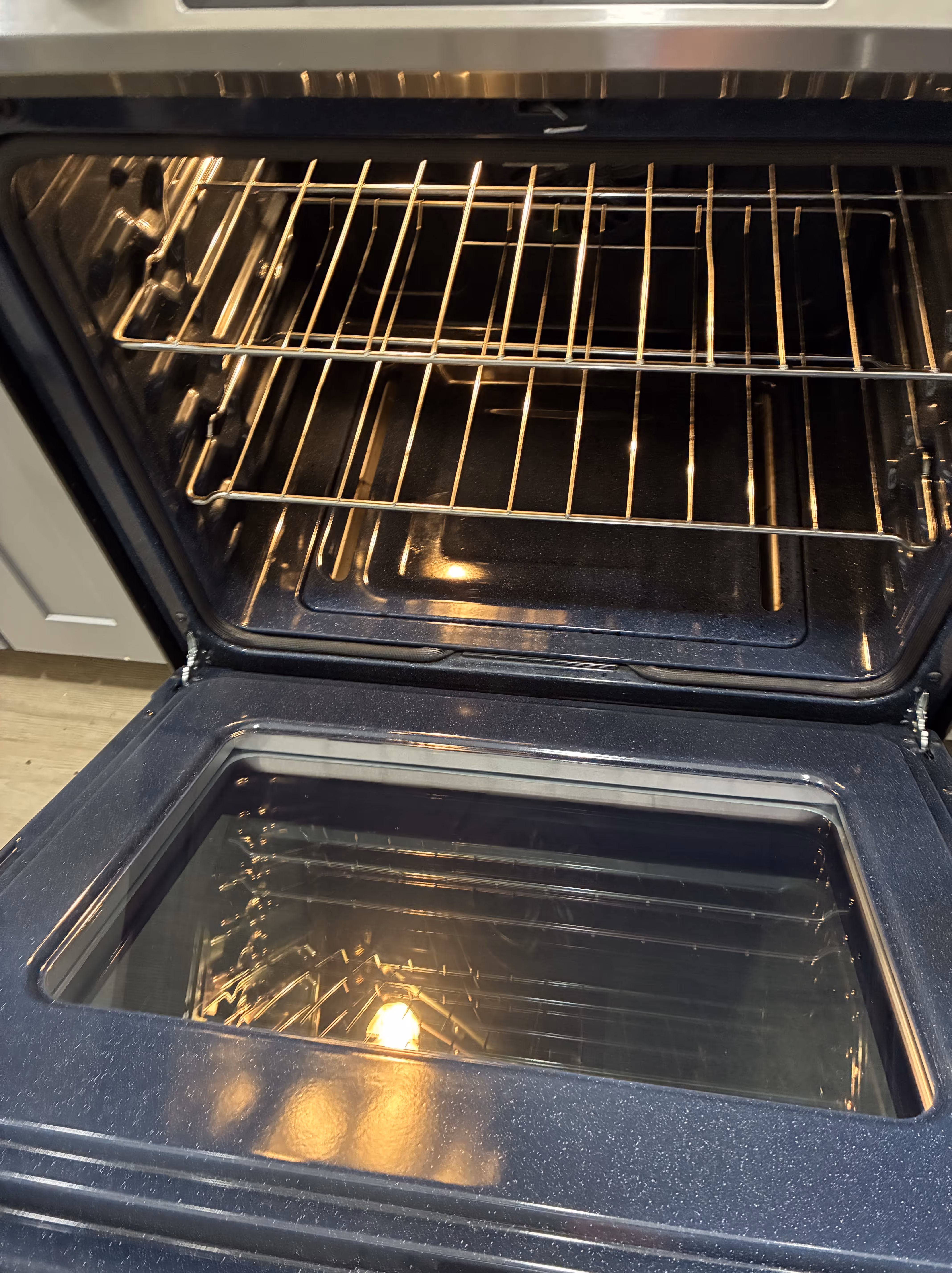 Stainless steel gas stove with black grates and digital clock displaying 9:45 with a black oven mitt hanging on the oven door handle.