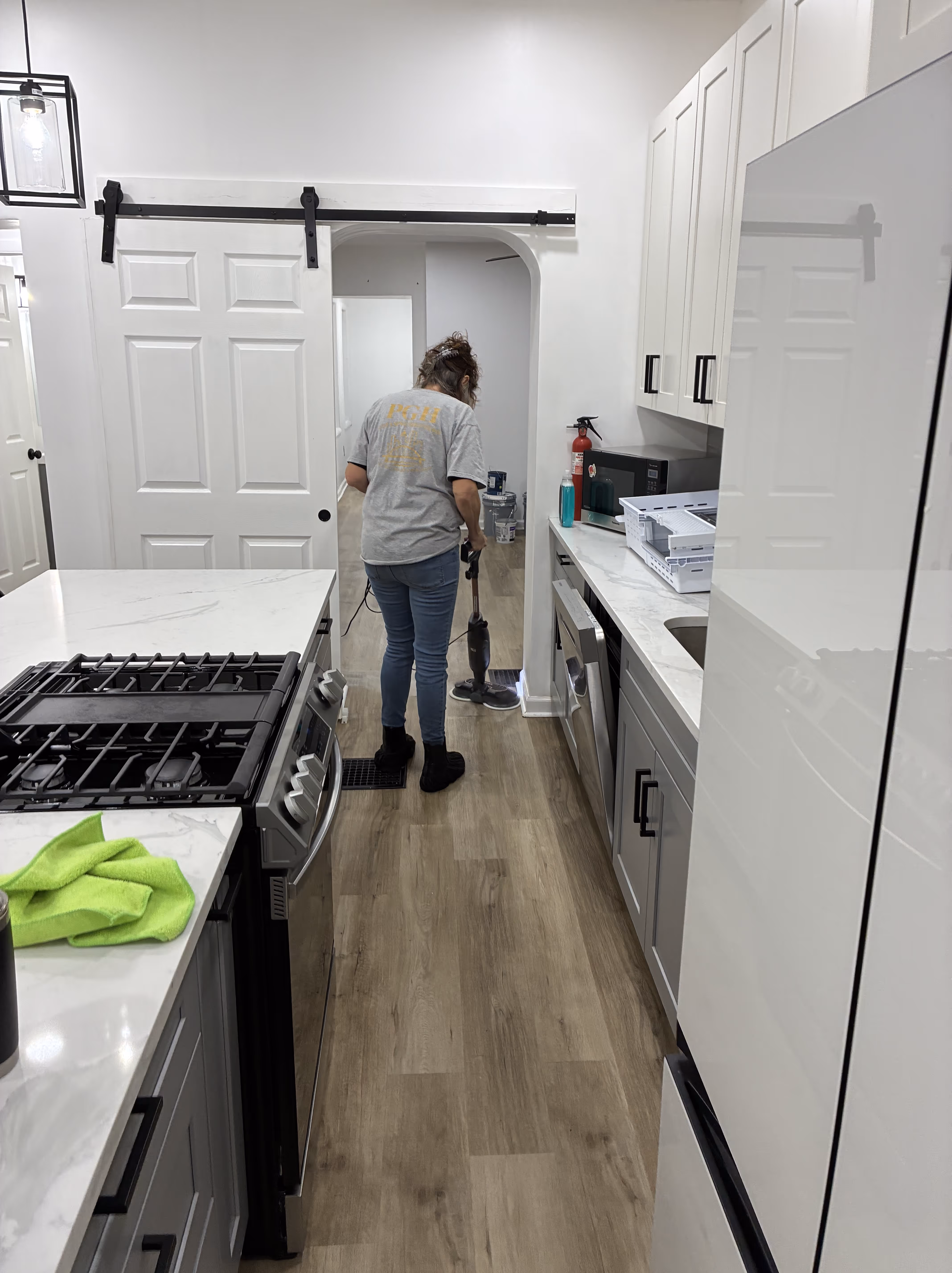 Person mopping a light-colored floor in a modern living room with a bucket of cleaning supplies in the foreground.