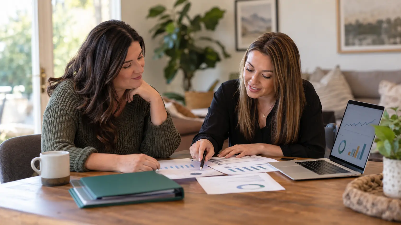 Parent and BCBA sitting together at a table, reviewing a laptop, printed progress charts, and a treatment folder in a calm, supportive consultation setting.