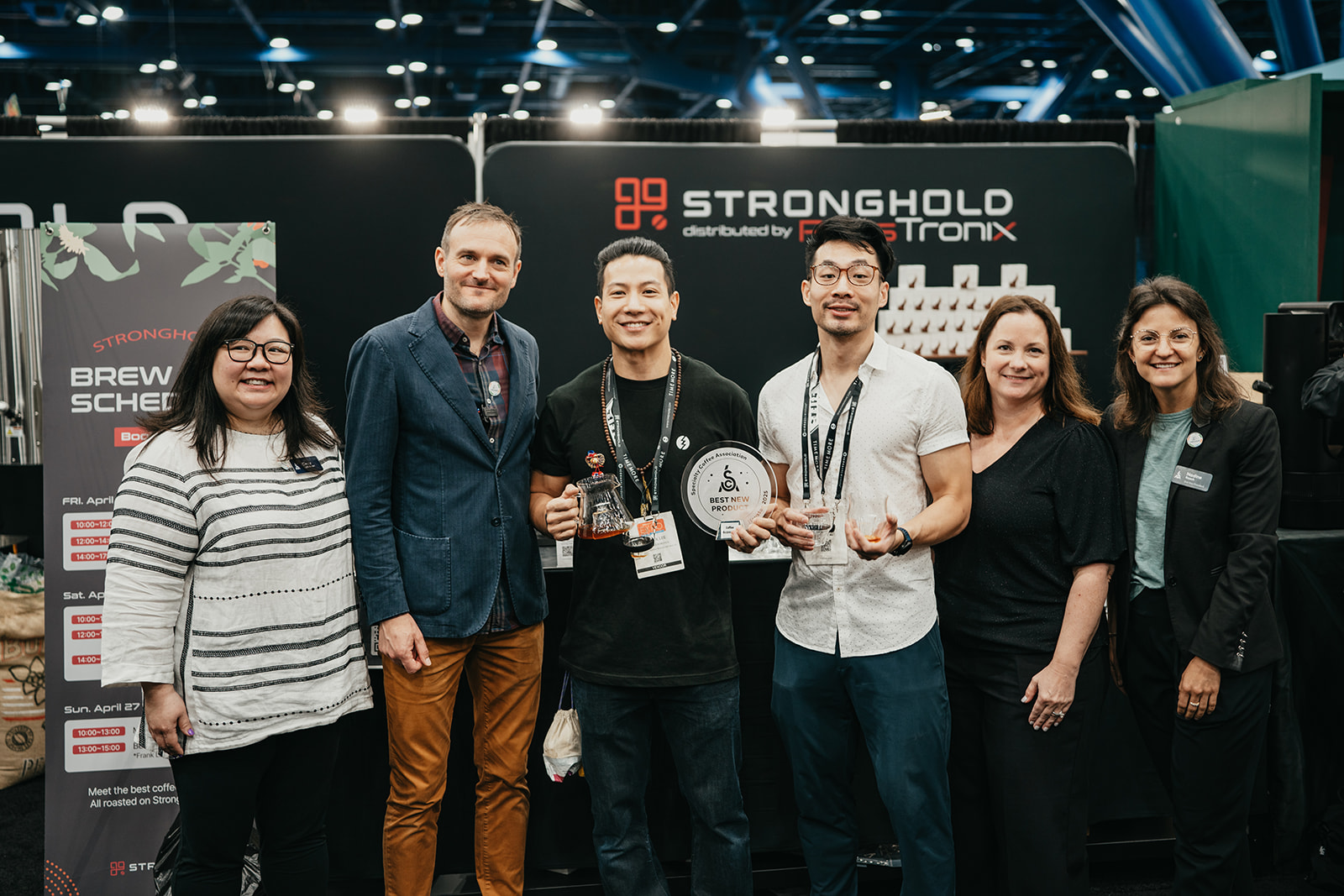Six people standing side by side at a Stronghold booth, two holding awards and smiling for the camera.