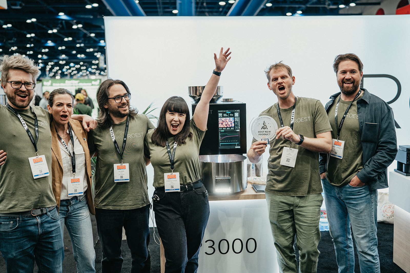 Six people in green Roest shirts smiling and celebrating around a coffee machine with a 'Best New Product' award plaque at a trade expo.