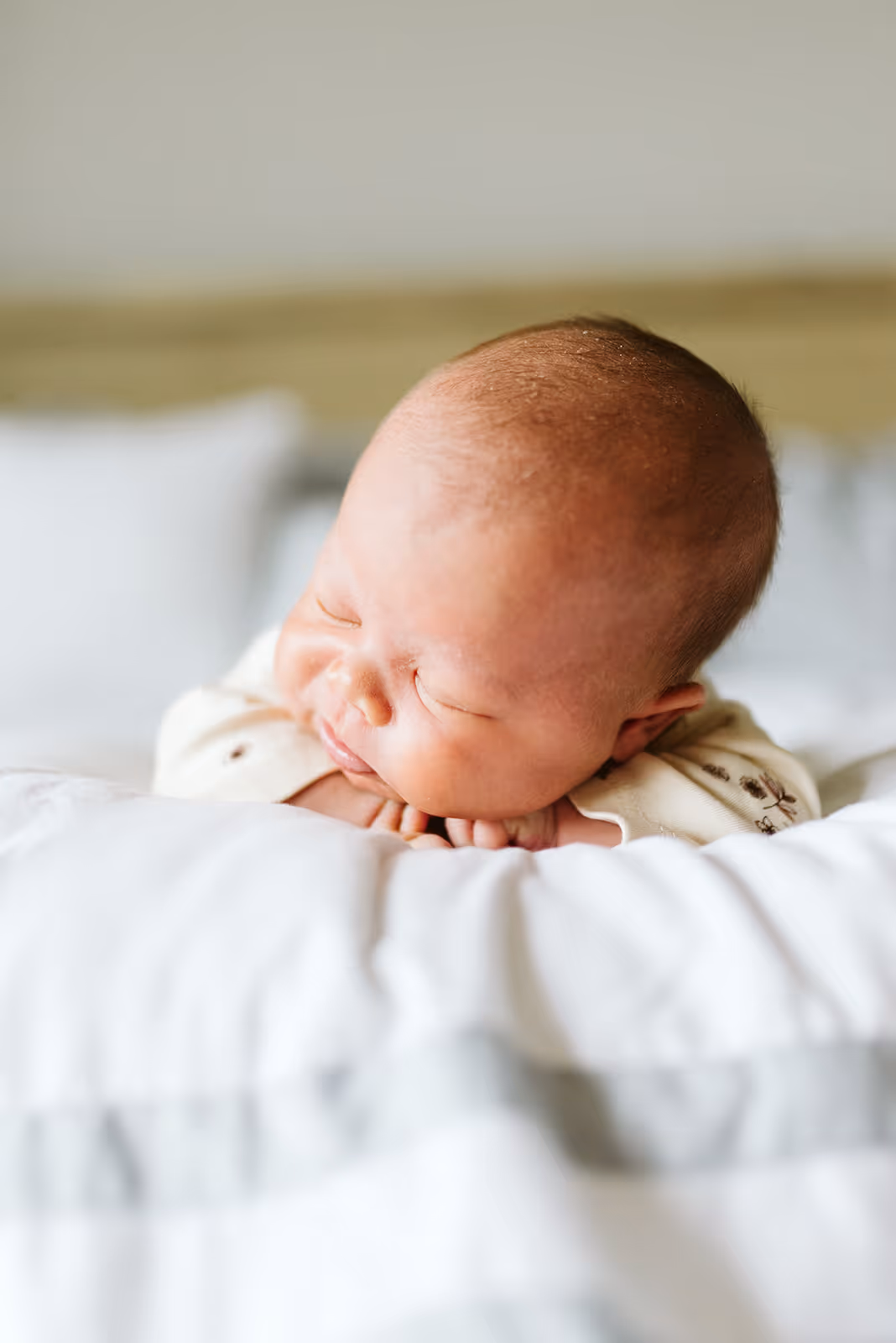 Sleeping newborn baby resting head on folded hands on a white blanket.