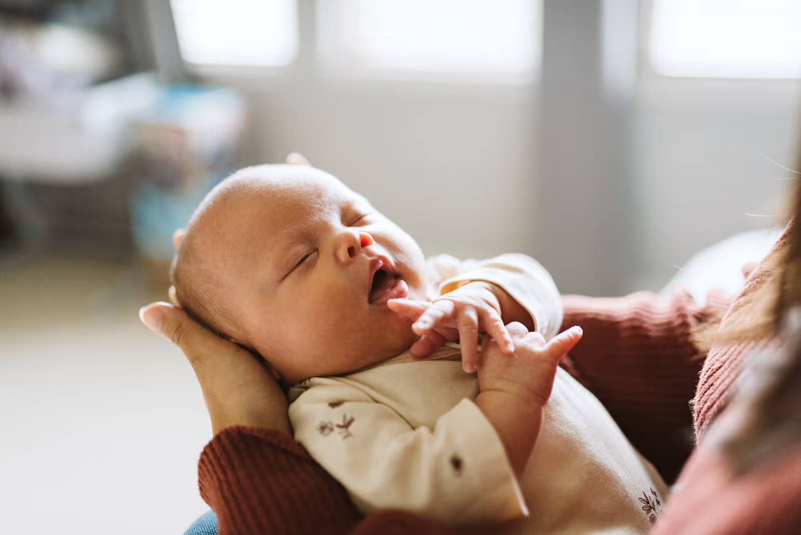 Sleeping newborn baby cradled in hands wearing a light-colored outfit.