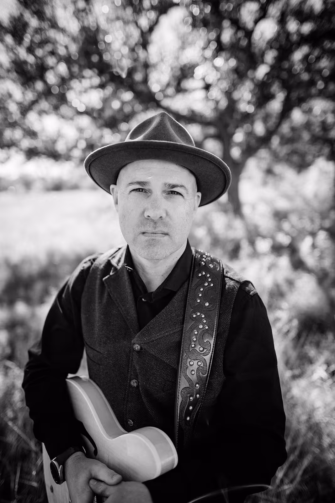 a man in a hat and vest holding a guitar