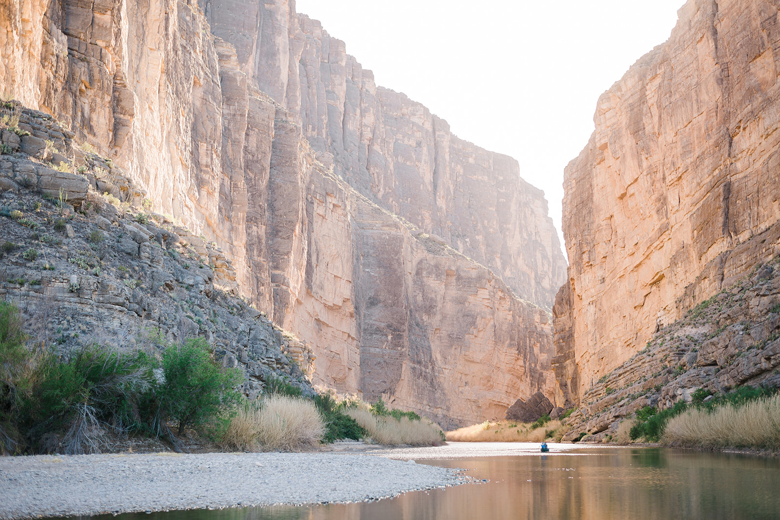 Large rocky canyon with steep cliffs and a calm river running through the bottom, featuring sparse vegetation along the riverbanks.