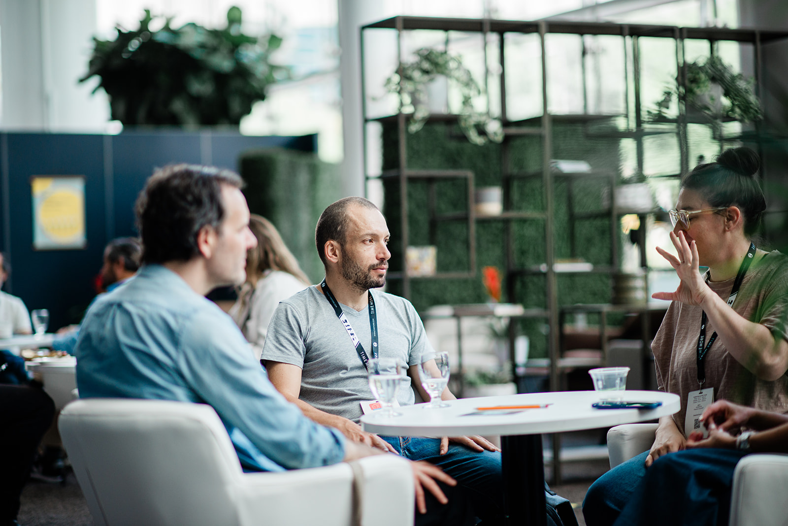 Three people having a discussion around a white table in a modern office space with plants in the background.