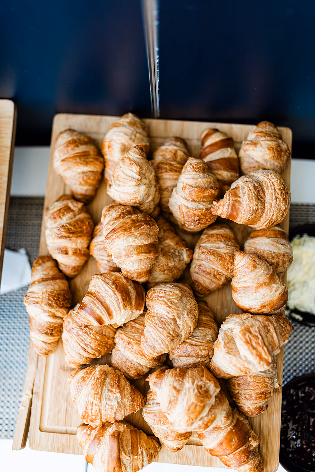 Wooden board filled with multiple golden brown croissants on a textured surface.