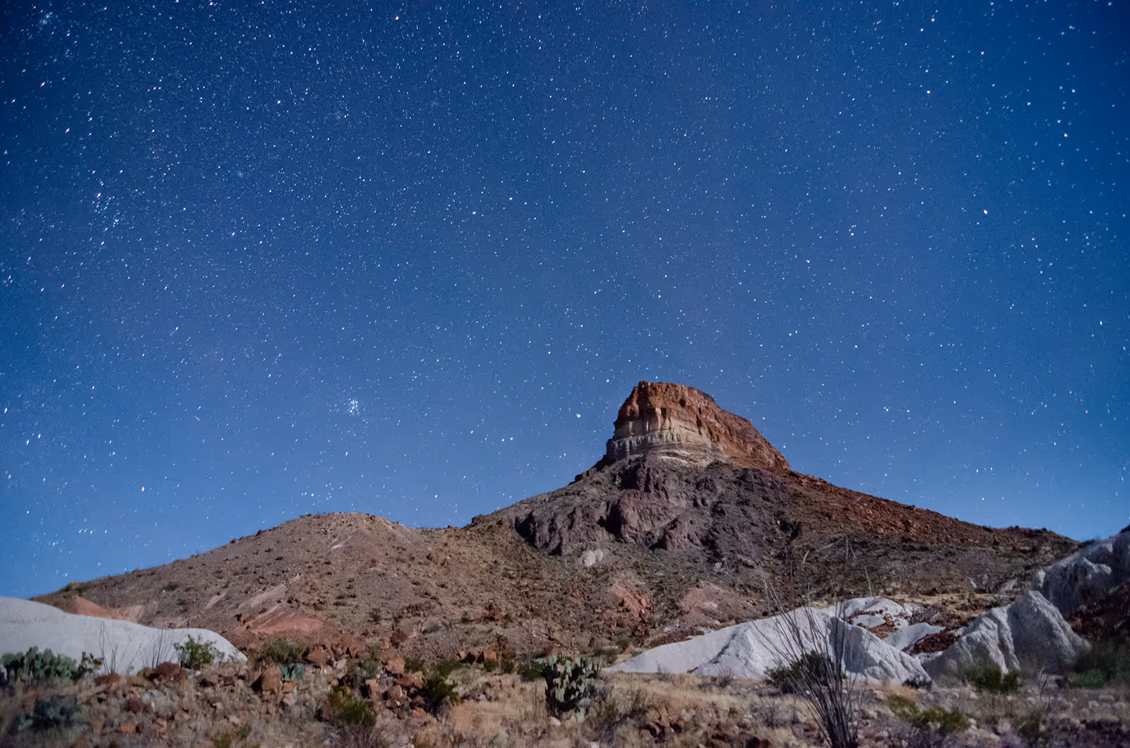 Rocky desert mountain under a clear, star-filled night sky.