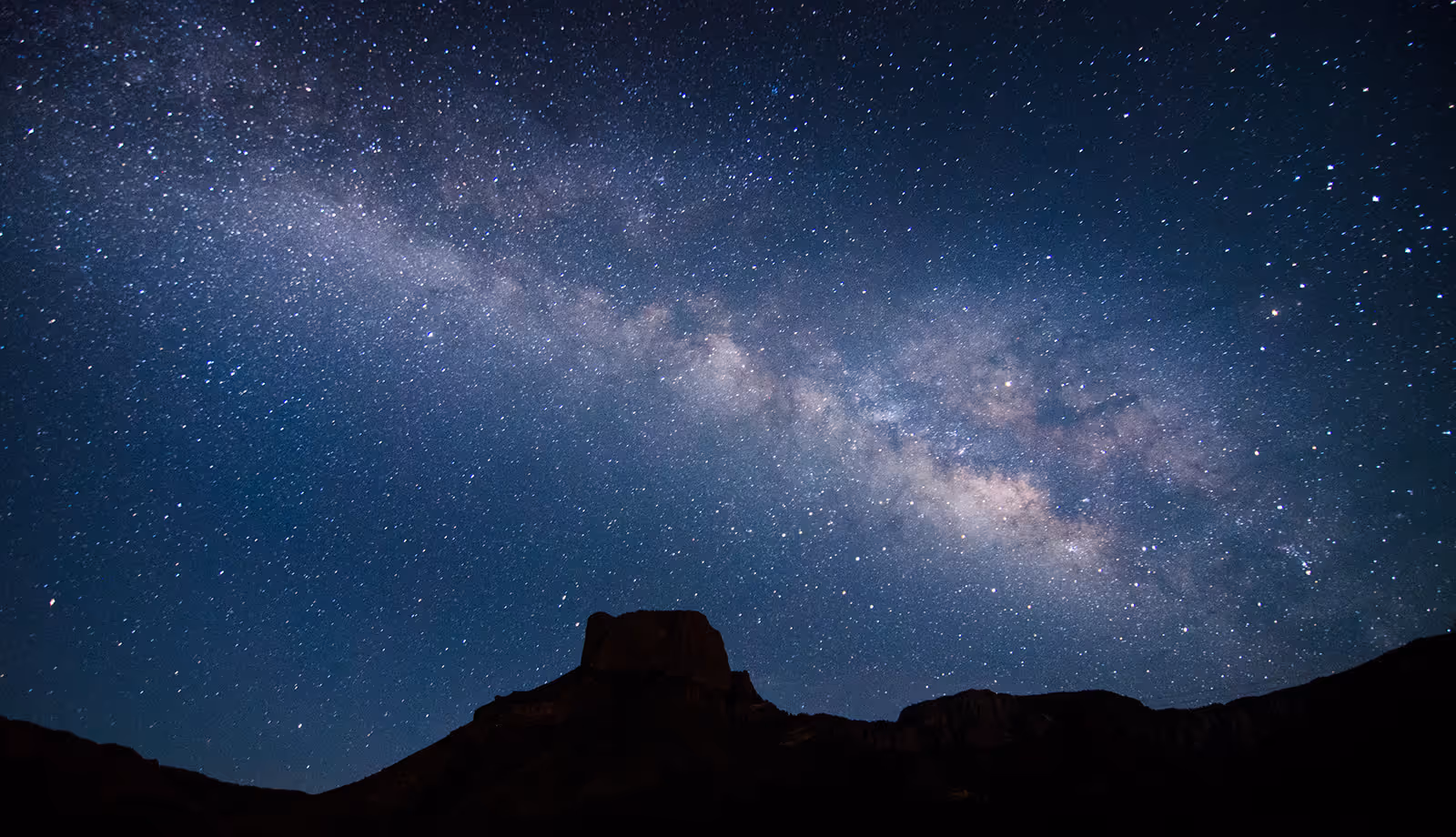 Milky Way galaxy visible in the night sky above a dark mountainous landscape silhouette.