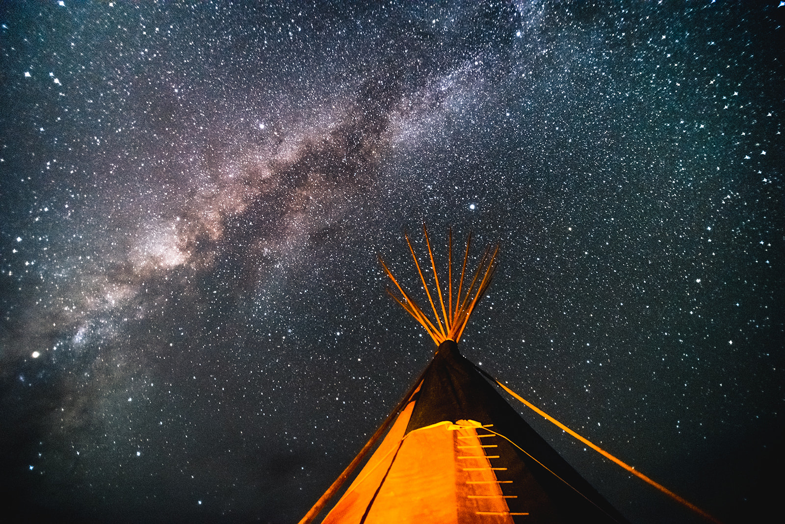 Night sky filled with stars and Milky Way arching above an illuminated tipi.