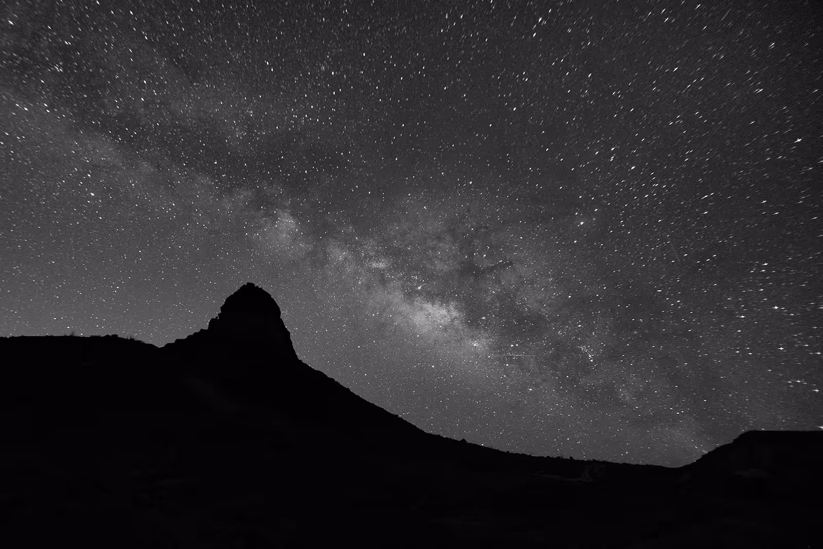 Silhouette of a mountain peak under a starry night sky with the Milky Way visible.