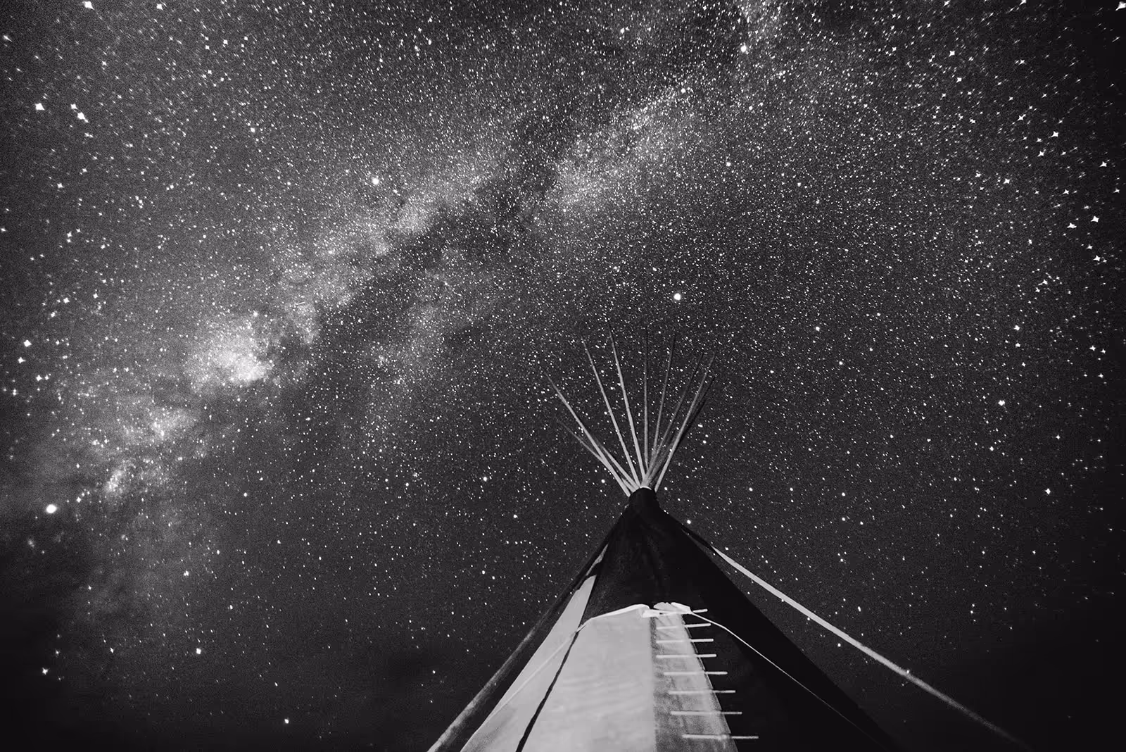 View looking up at a tipi with the Milky Way and a star-filled night sky in the background.