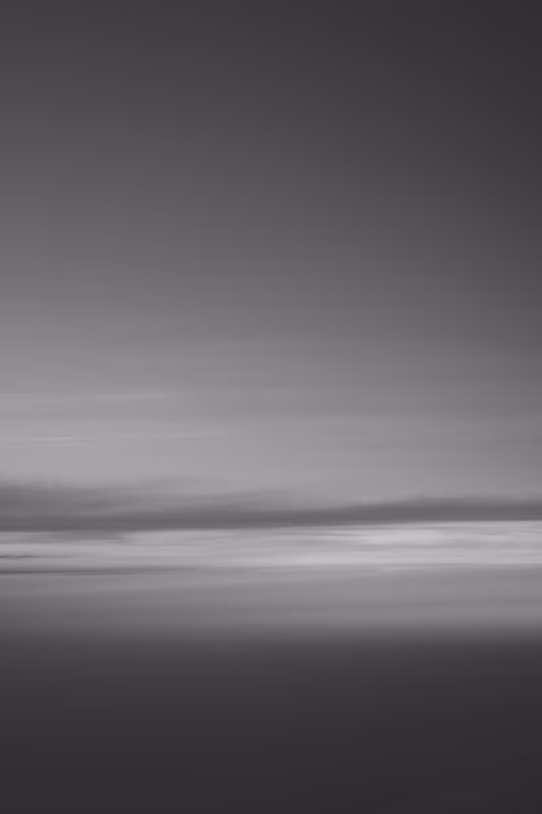 Black and white photo of a calm sky with layered clouds and a soft gradient from light to dark.